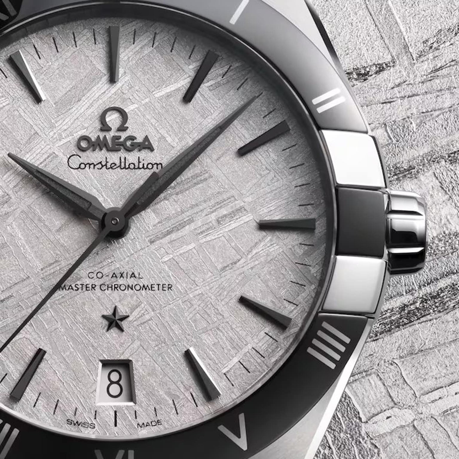 Close-up of an OMEGA Constellation watch featuring a textured silver dial, black hour markers, and a date window at 6 o’clock, set against a matching background.