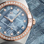 Close-up of an OMEGA Constellation watch with a blue meteorite-textured dial, diamond hour markers, and an 18K Sedna Gold bezel set with diamonds.