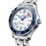 A close-up of the OMEGA Seamaster Diver Americas Cup 300M shows its blue bezel, white textured dial, and stainless steel bracelet. The watch features prominent minute markers and displays time and date.