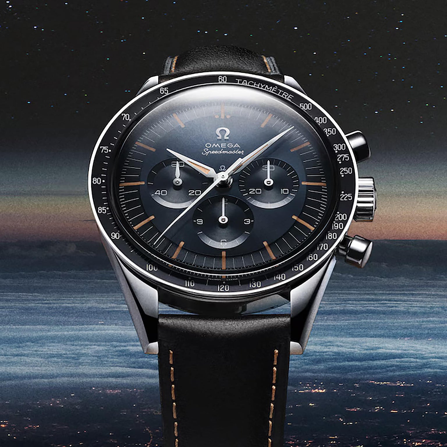 A close-up of the OMEGA Speedmaster First OMEGA in Space wristwatch with a black dial and leather strap, set against a twilight sky. The iconic tachymeter scale encircles the bezel.