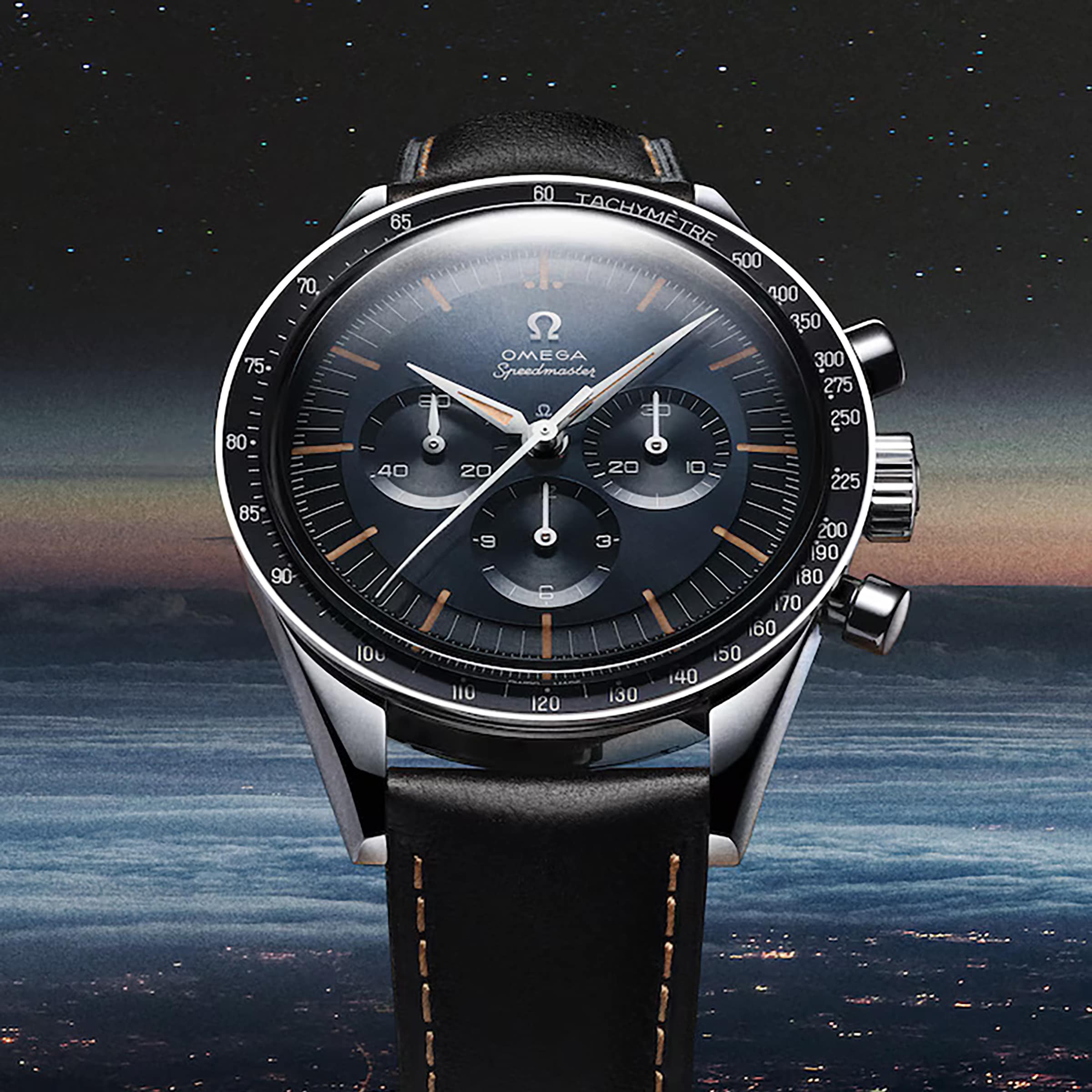 A close-up of the OMEGA Speedmaster First OMEGA in Space wristwatch with a black dial and leather strap, set against a twilight sky. The iconic tachymeter scale encircles the bezel.