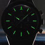 A close-up of an OMEGA Speedmaster Anniversary Series watch in darkness shows glowing green hour markers and hands on a faint dial, with the tachymeter scale subtly outlining the edge.