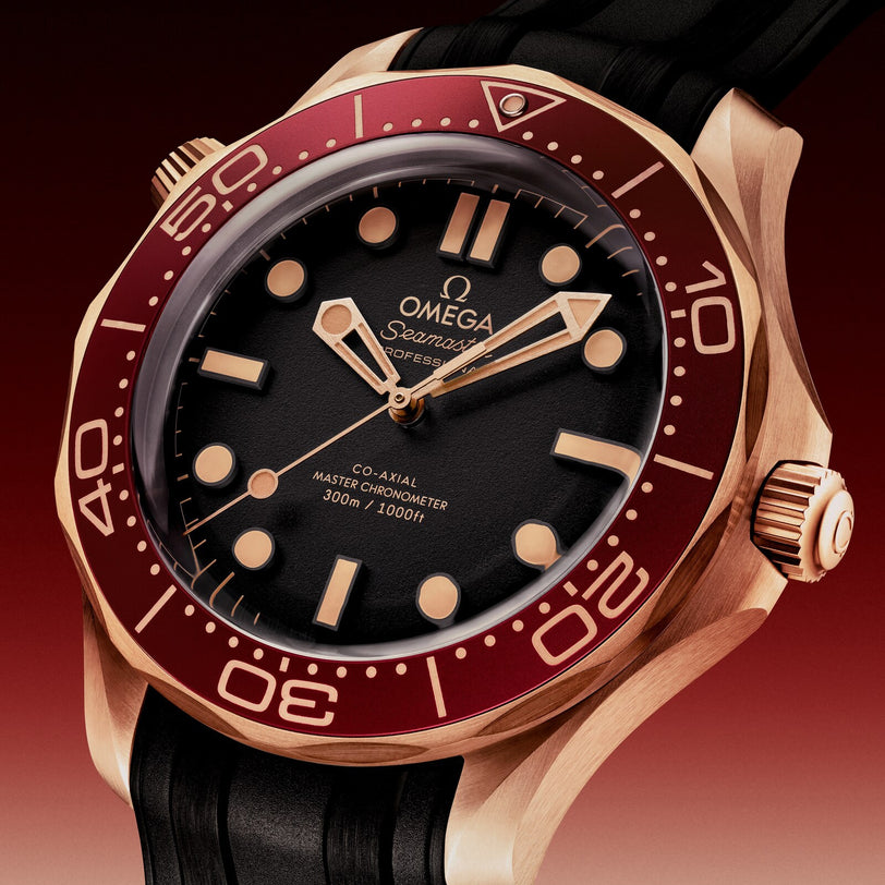 A close-up of the OMEGA Seamaster Diver 300M featuring a red bezel, Bronze Gold case, black dial and strap, showing the time at 10:09.