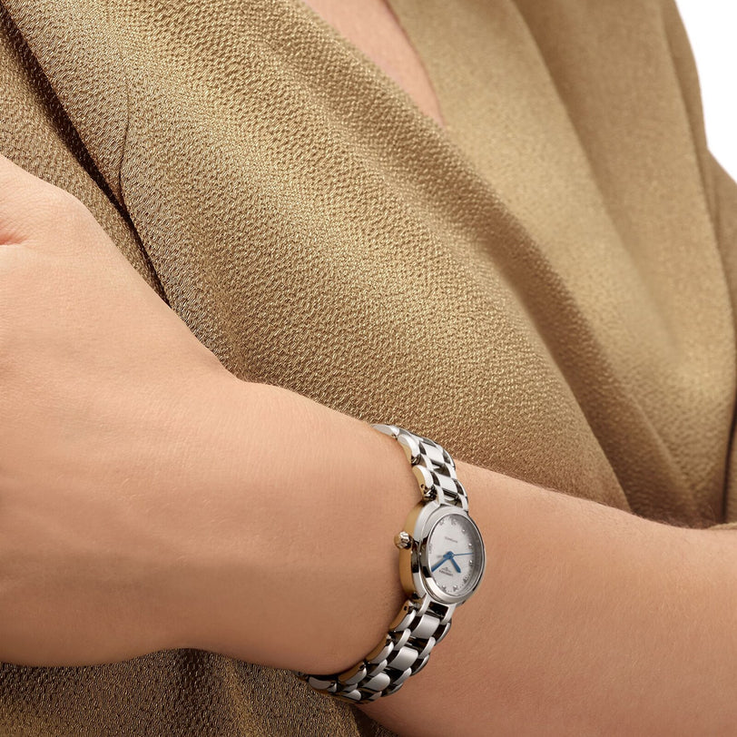 Close-up of a person wearing the Longines PrimaLuna watch, featuring a round diamond-set dial, paired with a textured beige top from the feminine collection.