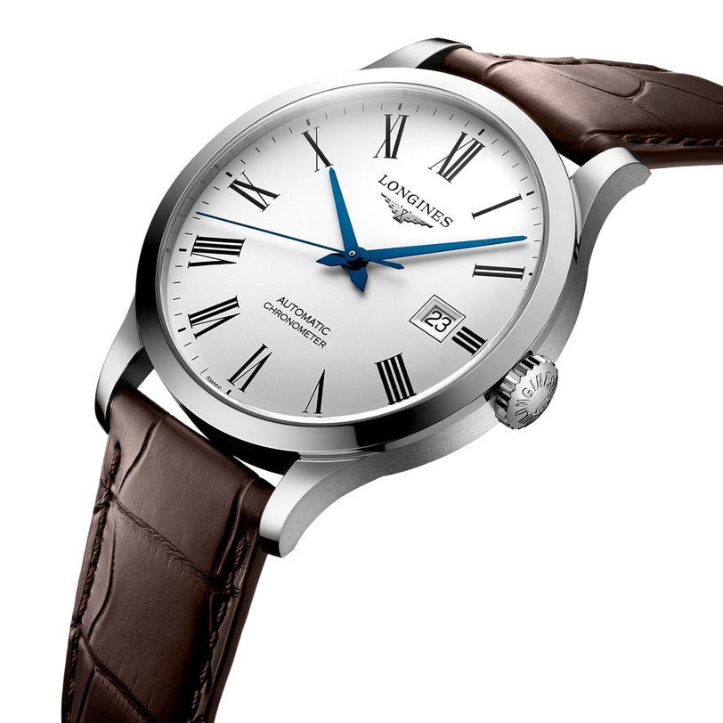 The Longines Record features a silver case, white dial with black Roman numerals, blue hands, date at 3 o’clock, brown leather strap, “Automatic Chronometer” inscription, and a silicon balance spring.