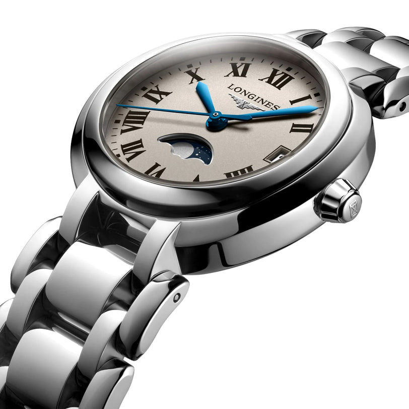 The Longines PrimaLuna Moonphase features a stainless steel case, white dial with blue hands, Roman numerals, a moonphase display at 6 o’clock, and comes on a metal link bracelet.