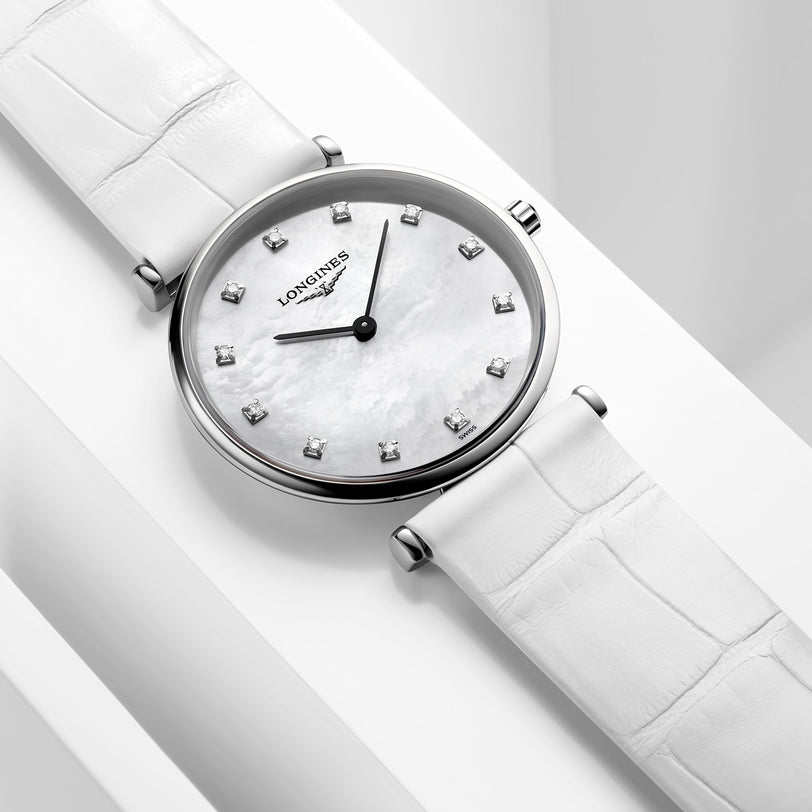 The Longines La Grande Classique de LONGINES wristwatch features a white leather strap, silver case, white mother-of-pearl dial with diamond hour markers, black hands, and an L420 quartz calibre movement.