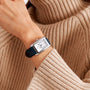 A person wears a Longines DolceVita rectangular silver watch with a black leather strap over the sleeve of a beige ribbed sweater.