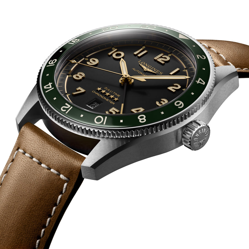A close-up of a Longines Spirit Zulu Time wristwatch featuring a black dial, gold numerals, green bezel, brown leather strap, and polished stainless steel case.