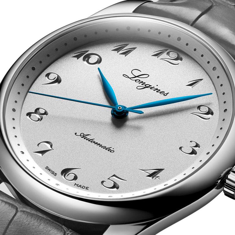 Close-up of a Longines Master Collection automatic watch featuring a silver dial, blue hands, Arabic numerals, leather strap, and a precise silicon balance-spring.
