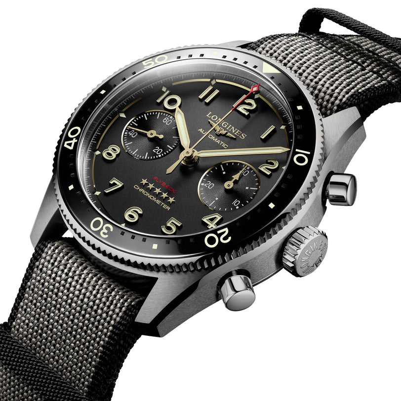 A close-up of the Longines Spirit Flyback Titanium, a pilot chronograph featuring a titanium case, black dial with three subdials, rotating bezel, and a textured fabric strap.