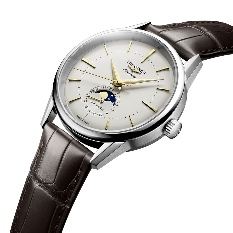 The Longines Flagship Heritage Moonphase wristwatch features a silver case, brown leather strap, gold hands and markers, and a moon phase display at 6 o’clock on a white dial.