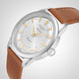 The Longines Conquest Heritage, a silver wristwatch with a white dial, gold hour markers, and brown leather strap, is shown at an angle on a light background—capturing classic Swiss watch precision.