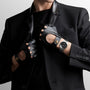 A person in a black suit and cutout leather gloves adjusts their jacket collar, showcasing the Longines Legend Diver watch on their left wrist.
