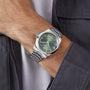 A person wearing a Longines Conquest watch with a green dial, Swiss Super-LumiNova accents, and date display rests their hand near a gray jacket.