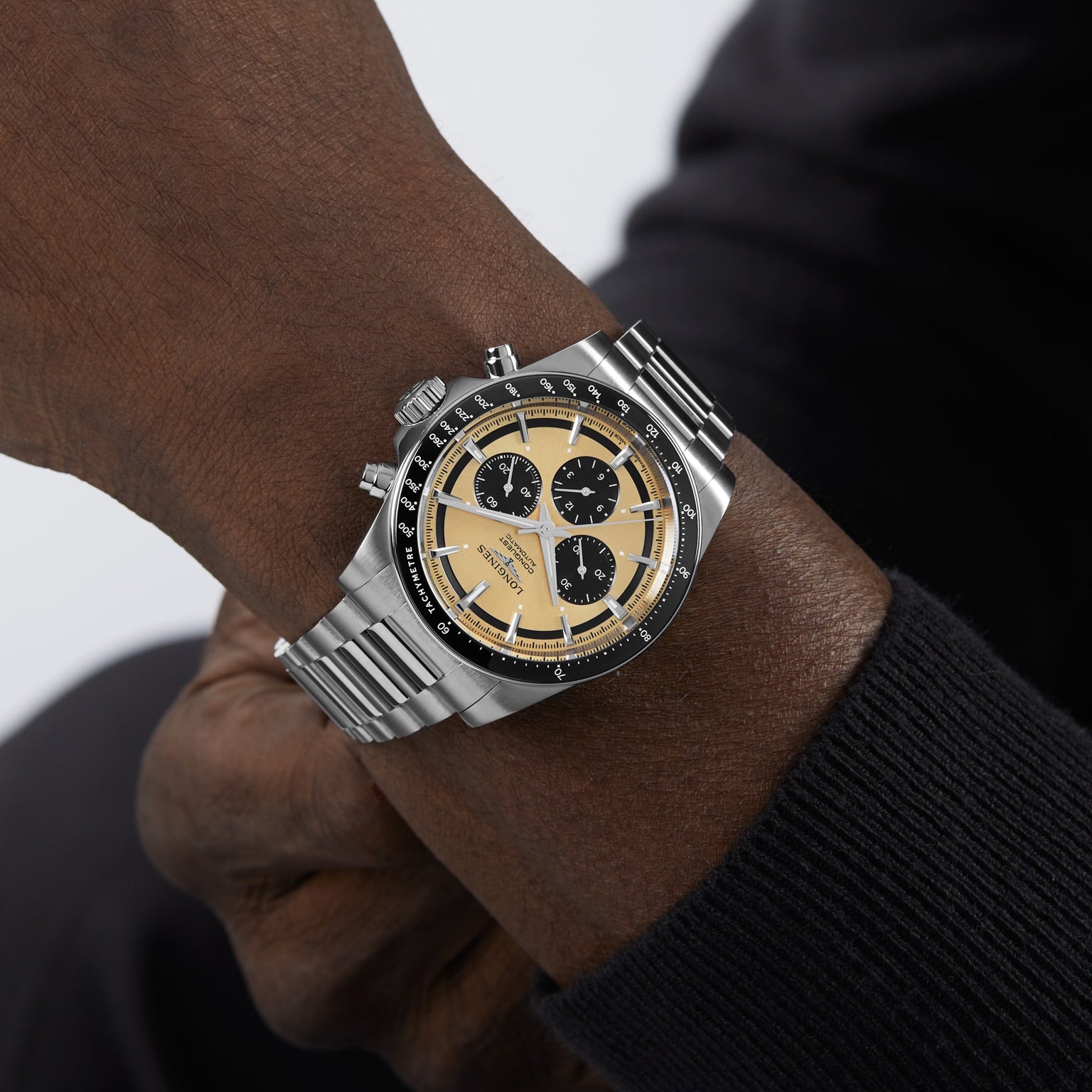 A person wearing a Longines Conquest Chronograph with a stainless steel case, beige and black dial, and metal bracelet, reflecting elegance and high performance.