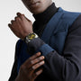 A person in a blue blazer and black turtleneck showcases a Longines HydroConquest watch with a silver case and gold face on their left wrist against a plain background.