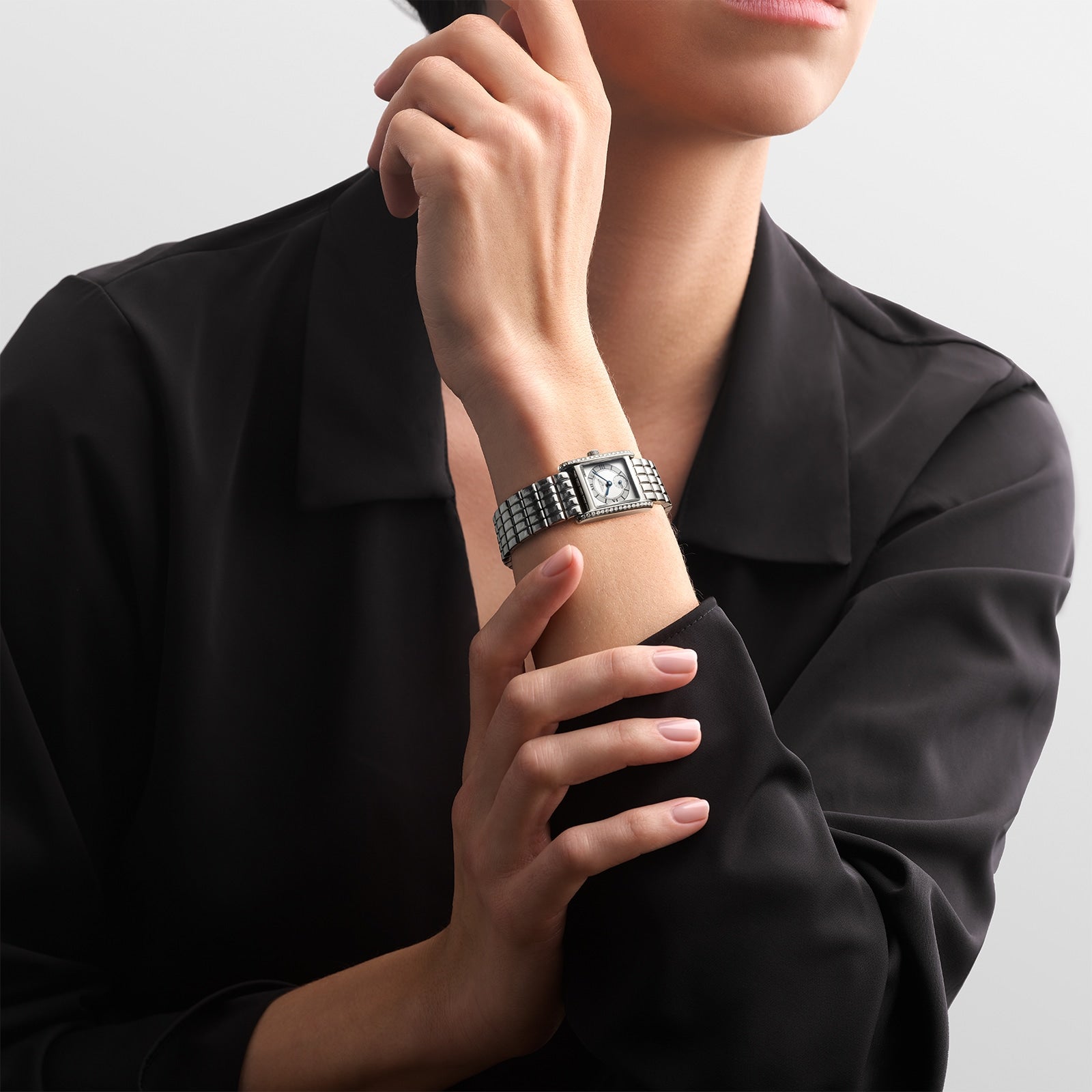A person in a black long-sleeve shirt wears a Longines Mini DolceVita with a rectangular face and stainless steel bracelet on their left wrist.