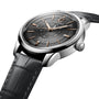A close-up of the Longines Conquest Heritage Central Power Reserve watch, featuring a black leather strap, black dial with Swiss SuperLumiNova®, rose gold hour markers, and a date display at 12 o’clock.