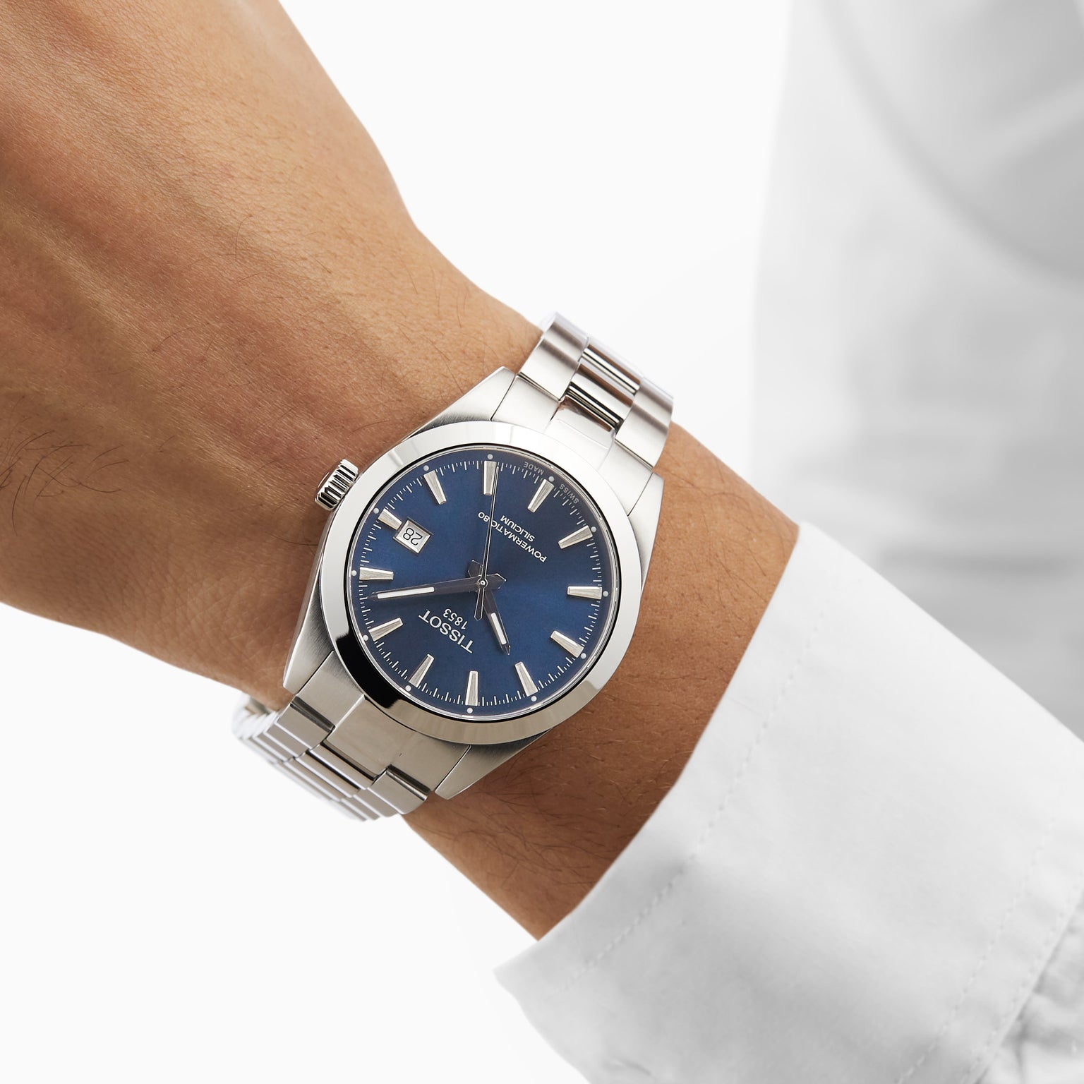 A person in a white long-sleeve shirt wears the Tissot Gentleman Powermatic 80 Silicium, featuring a blue dial, stainless steel case, and metal band.