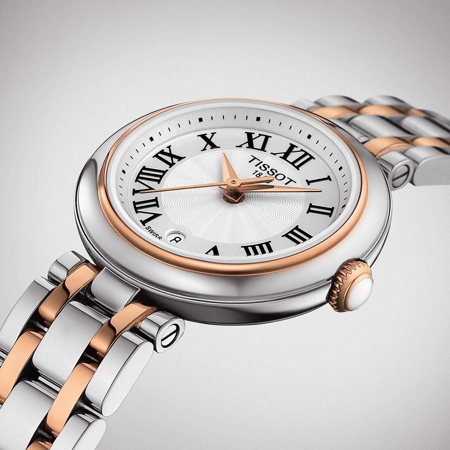 The Tissot Bellissima Small features a silver and rose gold PVD band, white dial with black Roman numerals, Swiss quartz movement, and a date window at 6 o’clock.