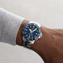 A person wearing a Tissot Seastar 1000 Powermatic 80 silver wristwatch with a blue face and white markings on their left wrist.