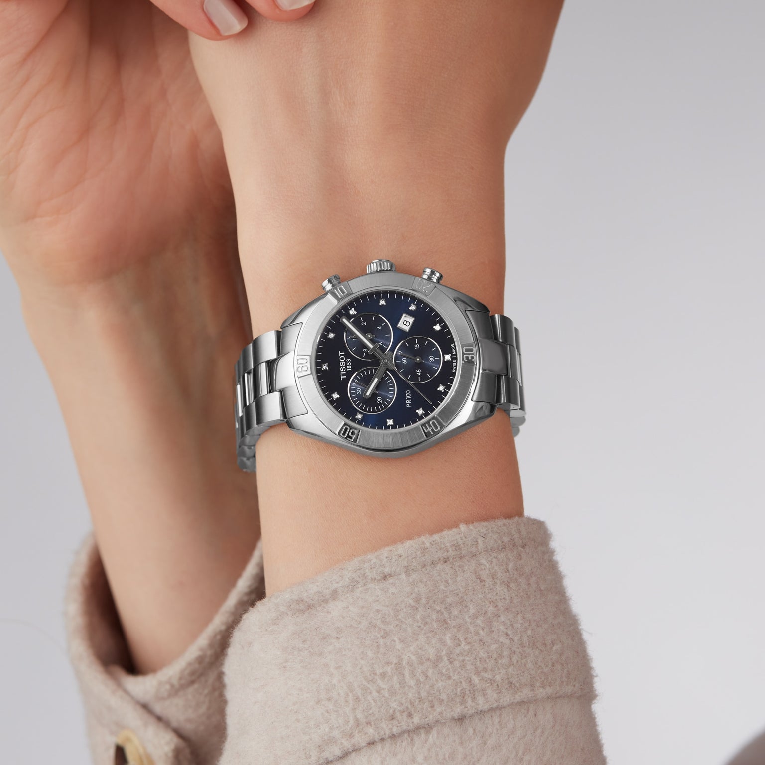 A close-up of the Tissot PR 100 Sport Chic Chronograph, featuring a silver case and blue dial, on a persons wrist.