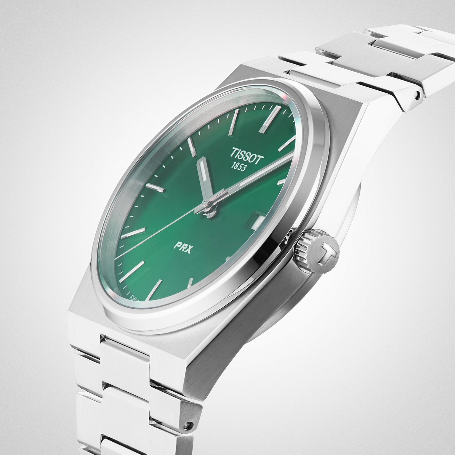 A Tissot PRX wristwatch with a green dial, silver hour markers and hands, and a stainless steel bracelet is displayed at an angle on a light background.