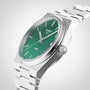 A Tissot PRX wristwatch with a green dial, silver hour markers and hands, and a stainless steel bracelet is displayed at an angle on a light background.
