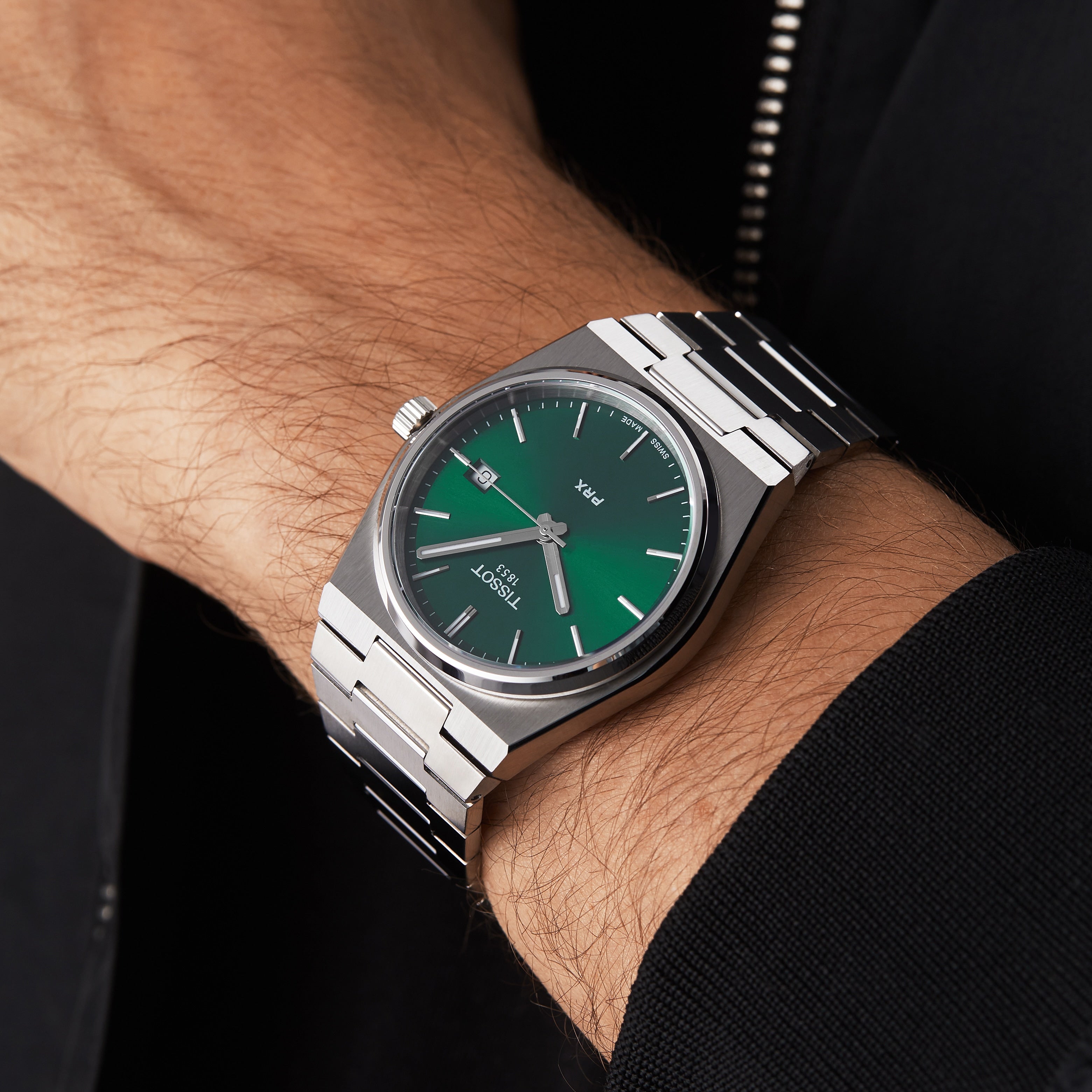 A Tissot PRX silver wristwatch with a green dial is worn on a persons left wrist.