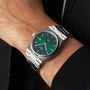 A Tissot PRX silver wristwatch with a green dial is worn on a persons left wrist.