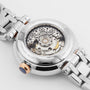 Close-up of the back of the Tissot Bellissima Automatic reveals its luxury and style with a transparent case, showcasing intricate gears and movement, complemented by a metal bracelet and a crown with a dark tip.