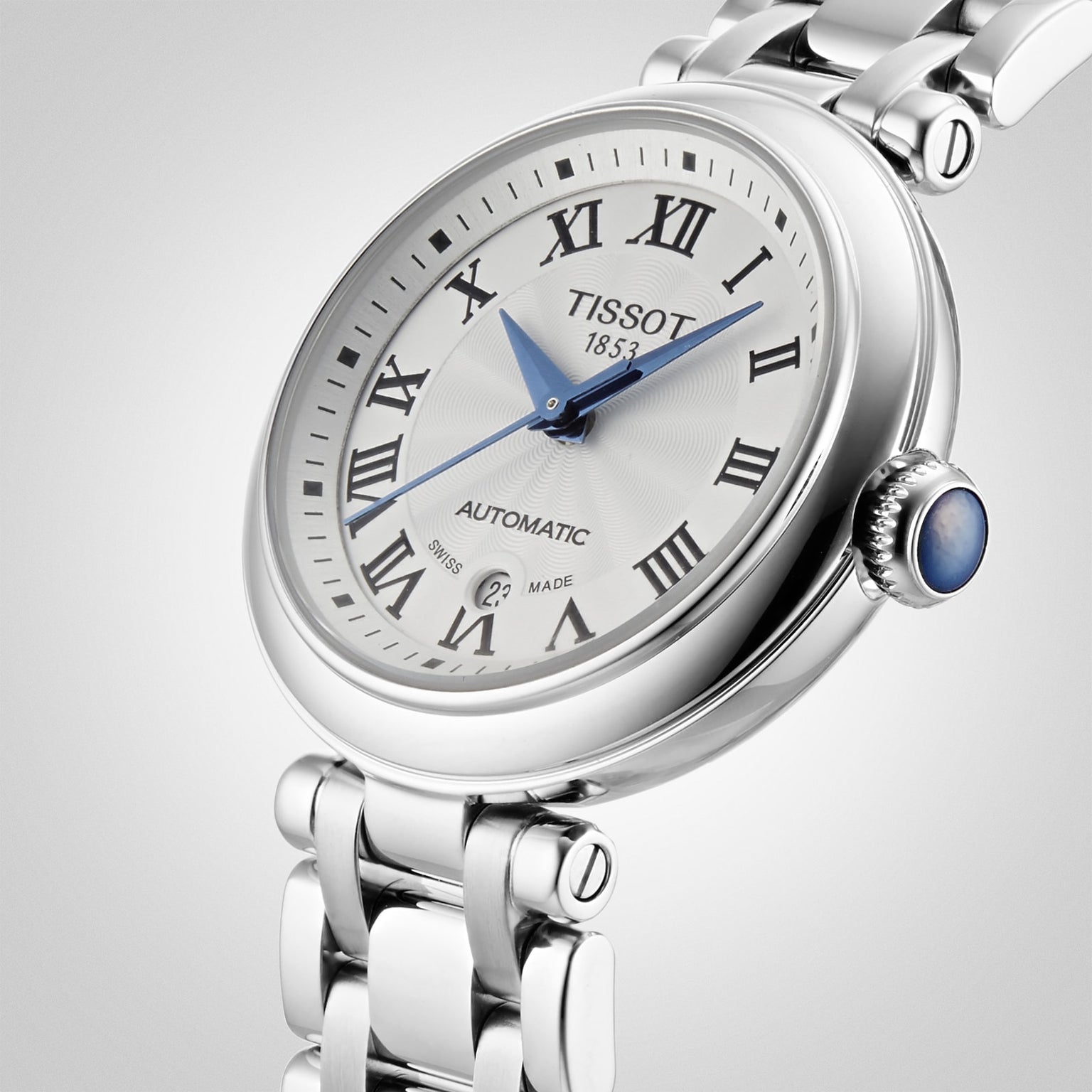 Tissot Bellissima Automatic wristwatch featuring a white dial with Roman numerals, blue hands, a date window at 6 o’clock, and a stainless steel bracelet.