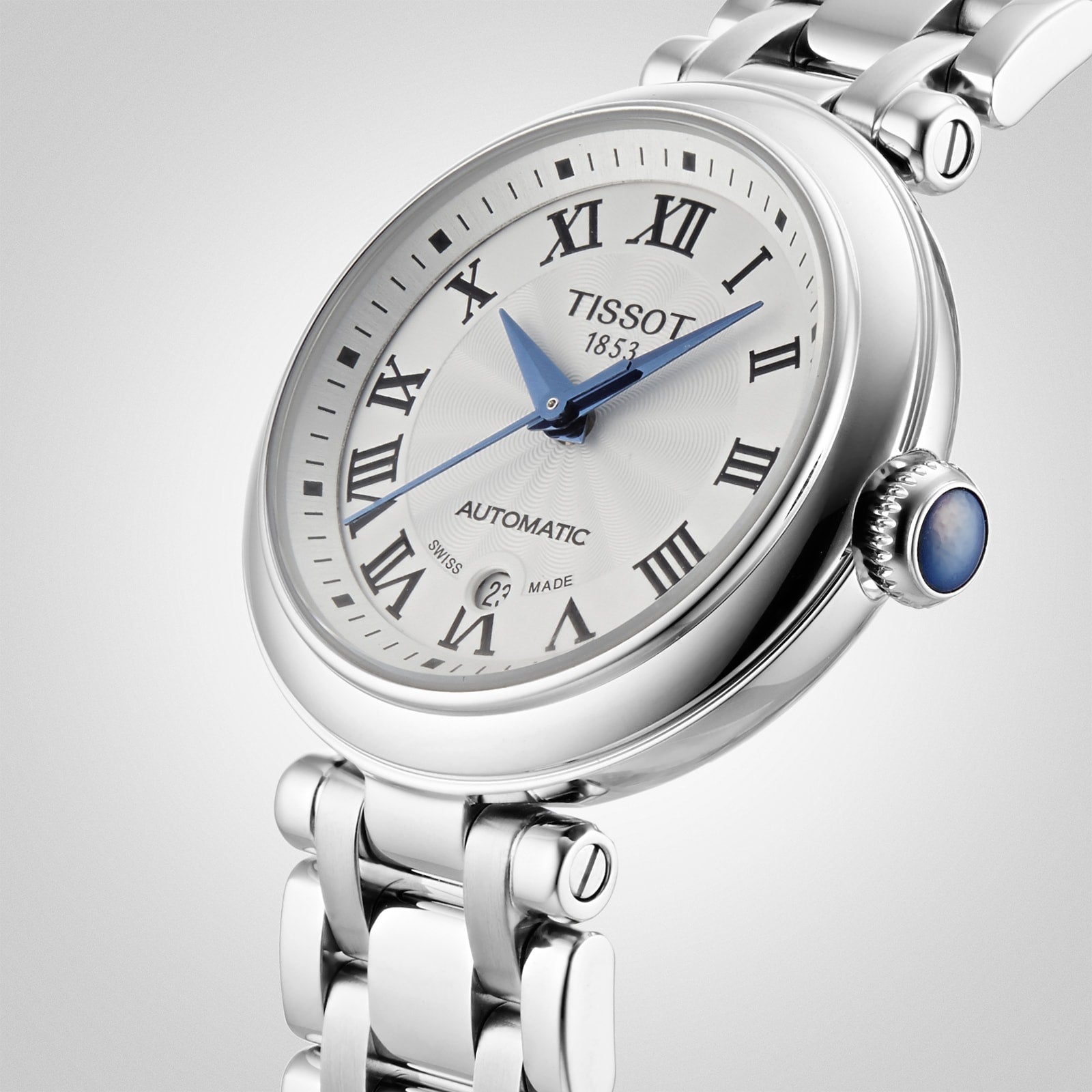 Tissot Bellissima Automatic wristwatch featuring a white dial with Roman numerals, blue hands, a date window at 6 o’clock, and a stainless steel bracelet.