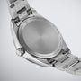 Close-up of the back of a Tissot PR 100 stainless steel wristwatch, featuring engravings detailing water resistance, scratch-resistant sapphire crystal, Swiss Quartz movement, and model information.