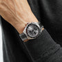 A person wearing a TAG Heuer Formula 1 Chronograph with a metal band, displayed against the sleeve of a dark sweater.