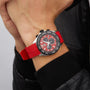 A person wearing a TAG Heuer Formula 1 Chronograph with a red band, black and red face, three subdials, tachymeter bezel, stainless steel case, paired with a black leather jacket.