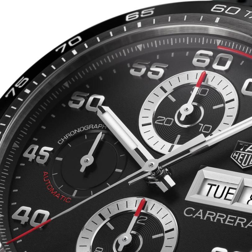 Close-up of the TAG Heuer Carrera Chronograph watch face, featuring hands, subdials, and date display. White and red numerals on black showcase its precision and endurance.