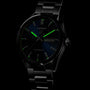 A black TAG Heuer Carrera Day-Date watch with luminescent green markers, calibre 5 automatic movement, and a day-date display reading Tuesday 8 is shown against a dark background.