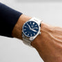 A TAG Heuer Carrera Day-Date stainless steel watch with a blue sunray dial, silver hour markers, and metal band is worn on a left wrist, featuring automatic movement and displaying the day and date.