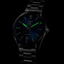 The TAG Heuer Carrera Date watch, featuring a dark dial, luminescent green markers, and a stainless steel bracelet, is showcased against a black background.