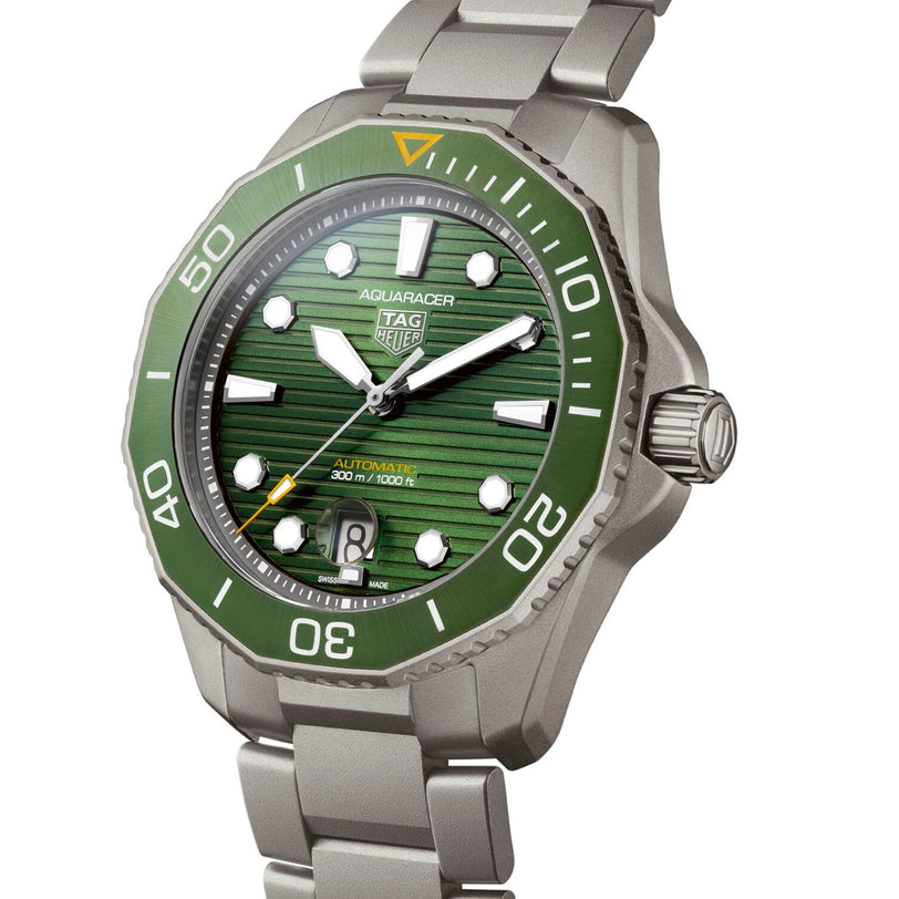 The TAG Heuer Aquaracer Professional 300 Date is a silver sports watch with a green dial and bezel, luminescent markers, stainless steel bracelet, and a date display at 6 oclock.