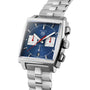 The TAG Heuer Monaco Chronograph features a silver case, blue square dial, two white subdials, date at 6 o’clock, vintage design, and a stainless steel bracelet.