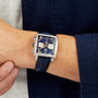 A person wearing the TAG Heuer Special Edition Monaco Gulf wristwatch, featuring a square face, blue strap and dial, two subdials, silver pushers, and powered by the automatic Heuer 02 movement.