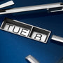 Close-up of the TAG Heuer Carrera Day-Date watch face showing TUE and 8 on a blue background, with metallic hands and markers—highlighting its Calibre 5 automatic movement.