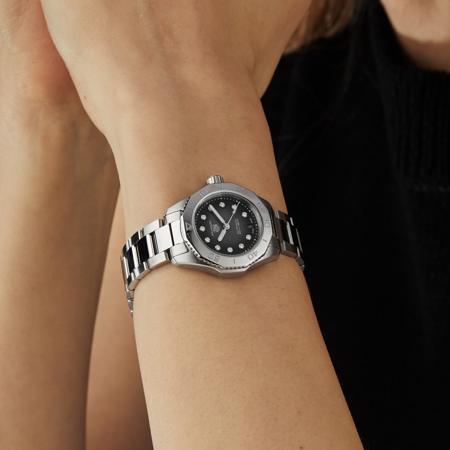 A TAG Heuer Aquaracer Professional 200 Date with a black mother-of-pearl dial and silver accents is worn on a person’s left wrist.