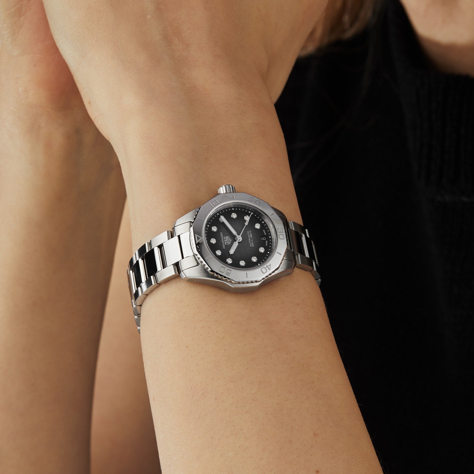 A TAG Heuer Aquaracer Professional 200 Date with a black mother-of-pearl dial and silver accents is worn on a person’s left wrist.