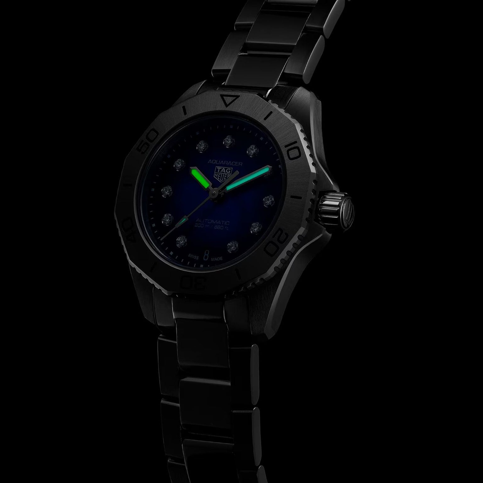 The TAG Heuer Aquaracer Professional 200 Date sports watch features a black stainless steel case and band, with a luminescent green minute hand and blue hour hand, shown against a dark background.