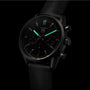 The TAG Heuer Carrera Chronograph features a black dial, two subdials, luminous green hands and markers, a Calibre HEUER 02 movement, and a black leather strap.