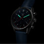 The TAG Heuer Carrera Chronograph features a black dial, luminous hands and markers, Calibre Heuer 02 movement, and a blue leather strap, displayed against a black background.